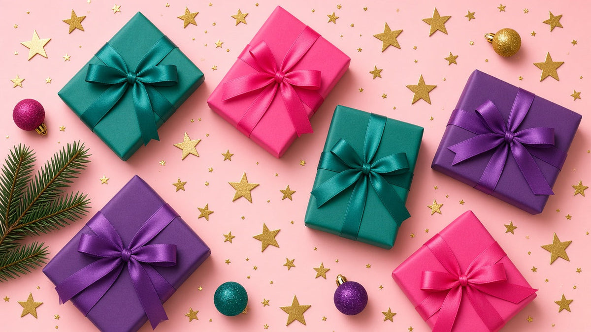 Gift boxes wrapped in purple, teal and pink paper with satin bows on a pink background with gold stars